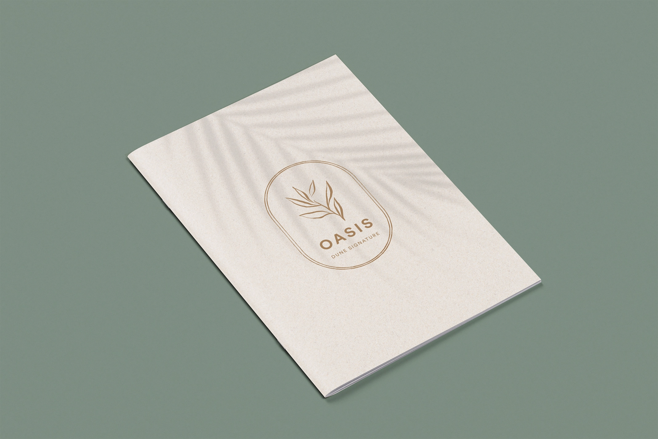 Dune Signature Oasis brochure, featuring a light-coloured cover with a subtle palm tree shadow pattern and a gold oval logo containing a leaf motif and the text 'OASIS DUNE SIGNATURE'. The brochure is shown at an angle on a grey-green background. This image exemplifies luxury property brochure design, using natural imagery and a sophisticated logo to reflect the villas' proximity to the ocean and their beautiful surroundings.