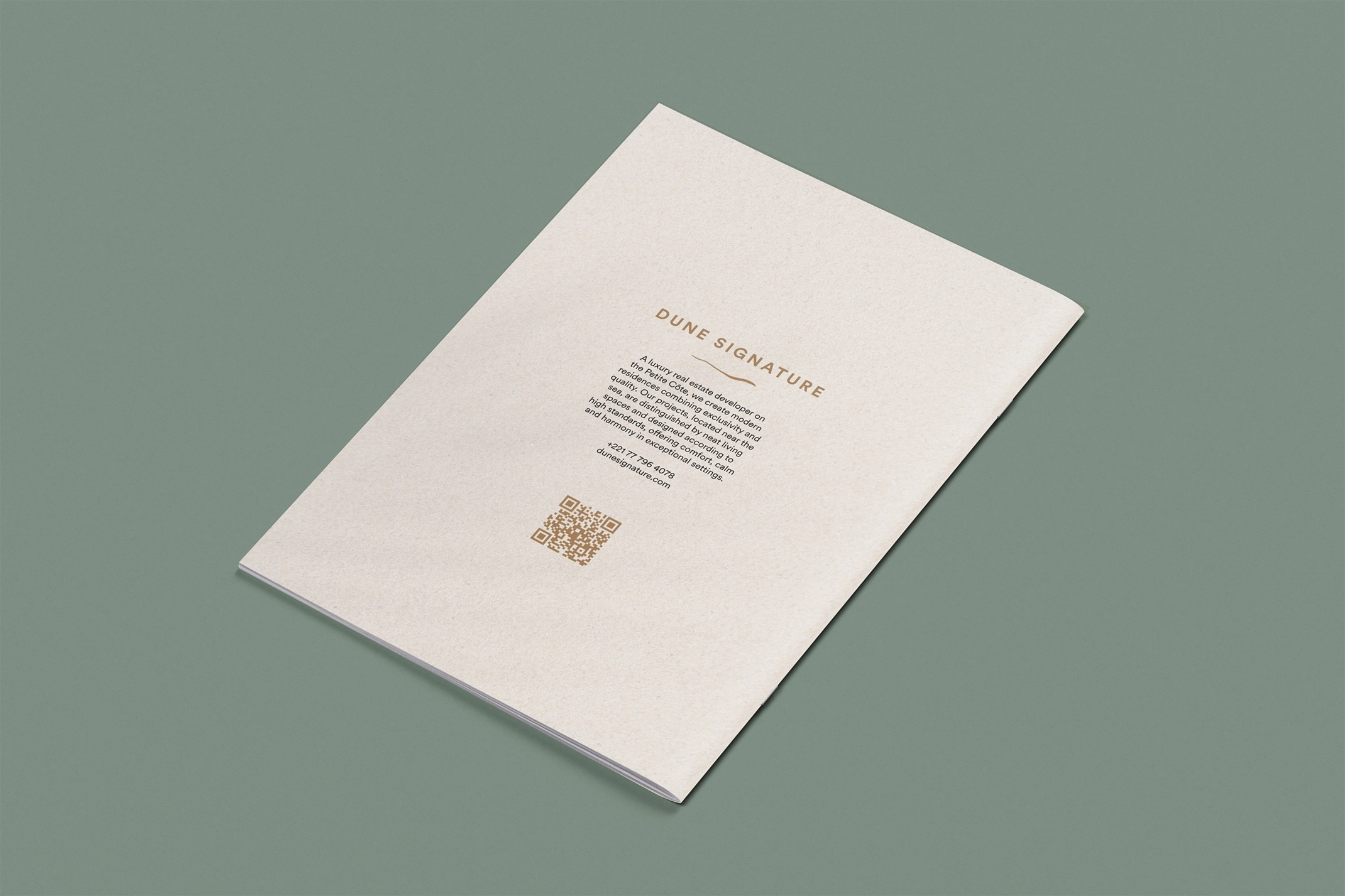 Back cover of the Dune Signature Oasis brochure, featuring the text 'DUNE SIGNATURE' at the top, followed by a paragraph of descriptive text about the company. A gold QR code is visible at the bottom left, and contact information is listed at the bottom right. The brochure is shown at an angle on a grey-green background.