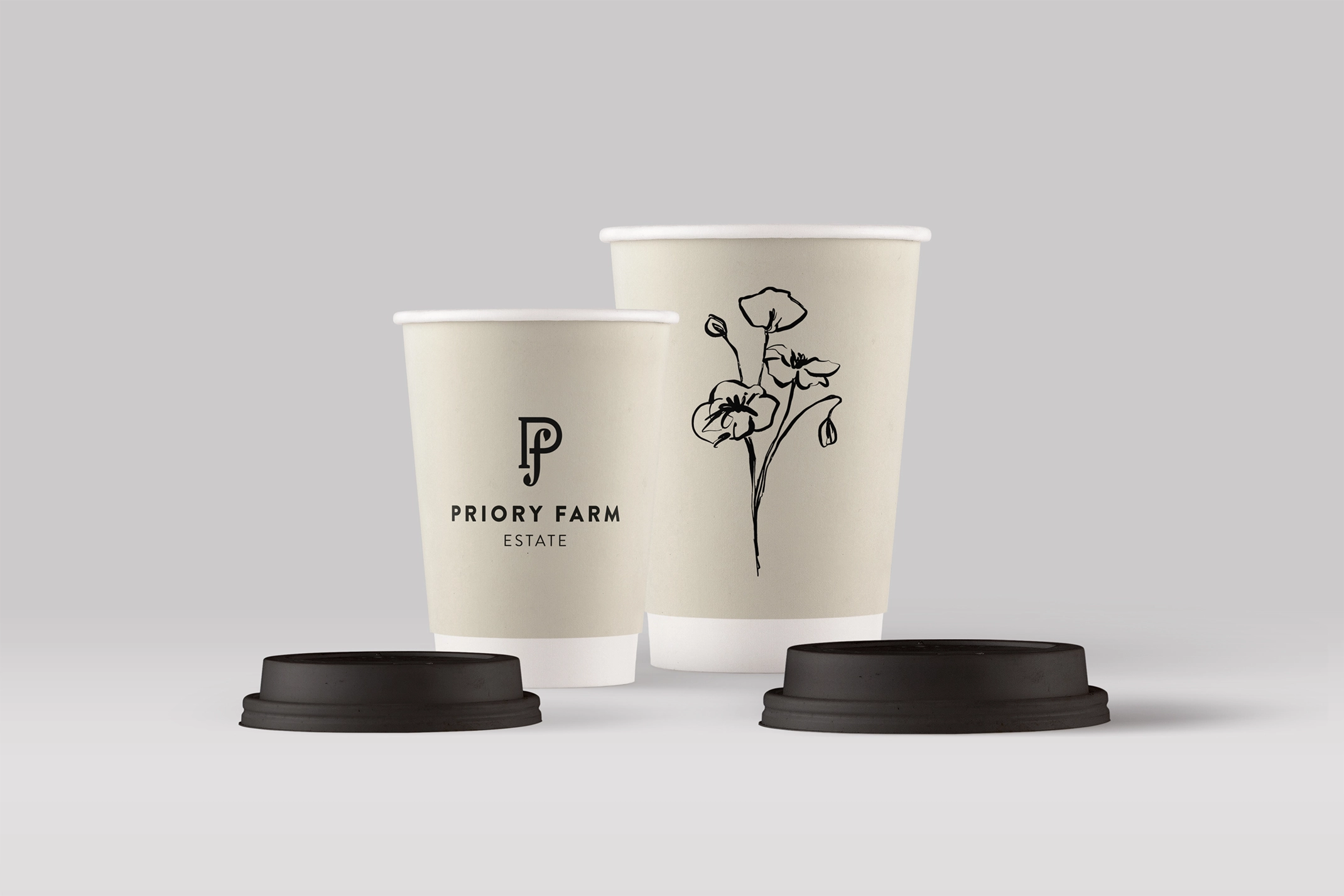 Two Priory Farm Estate coffee cups on a light grey background. The smaller cup features the 'P f' monogram and the words 'PRIORY FARM ESTATE', while the larger cup displays a black line-art illustration of a stylised flower.